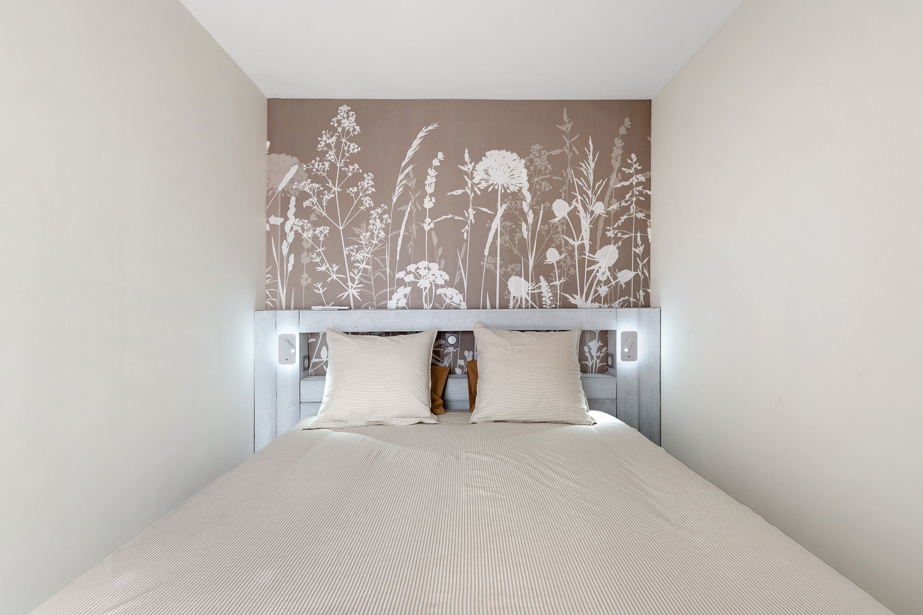 Ein Schlafzimmer mit einem Bett, zwei Kissen, einem Nachttisch und einer Wand mit einem Blumenmuster.