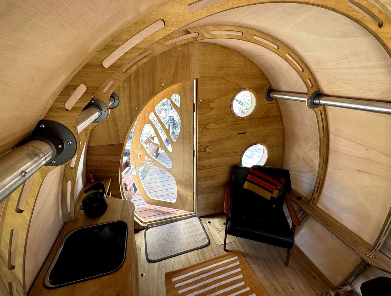 A compact, circular interior with a wooden finish, a small seating area, a sink, and a window providing natural light.