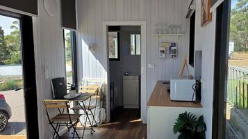 A compact room with a kitchenette, a dining area with a table and chairs, and a view of the outdoors.