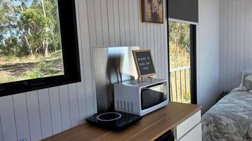 A room with a bed, a desk with a microwave, a sign reading 'Welcome to River Gun Lodge', and a window with a view of trees.