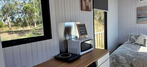 Una habitació amb un llit, un escriptori amb microones, un cartell que diu 'Welcome to River Gun Lodge' i una finestra amb vistes als arbres.