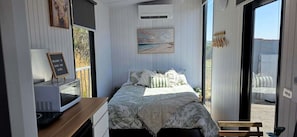 A bedroom with a bed, a desk, a chair, a window, and a door.