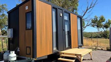 A compact, modern structure with a wooden exterior, a sliding door, and a small outdoor seating area.