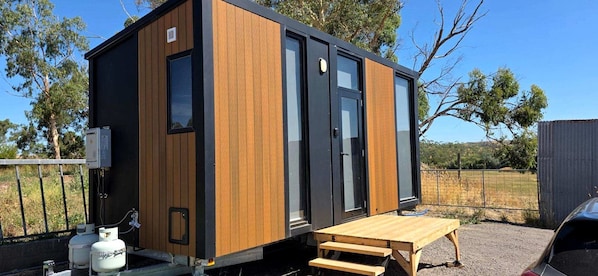 Una construcció compacta i moderna amb façana de fusta, una porta corredissa i una petita zona d'estar a l'exterior.