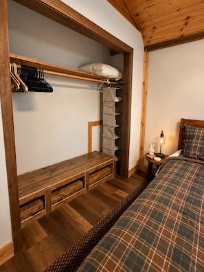 A bedroom with a bed, a wooden bench, a shelf with clothes, and a bedside table with a lamp. - Stunning Luxury Chalet with Attached Garage (Bessemer)