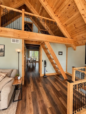 A spacious loft-style room with a high ceiling, wooden beams, and a staircase leading to an upper level. - Stunning Luxury Chalet with Attached Garage (Bessemer)