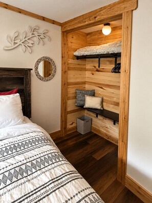 Ein Schlafzimmer mit einer Wand aus Holzlatten, einem Bett mit gemusterten Betttextilien, einem runden Spiegel und einer Pendelleuchte.