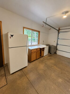 A compact kitchen with a refrigerator, wooden cabinets, a window, and a garage door. - Stunning Luxury Chalet with Attached Garage (Bessemer)