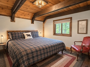 A bedroom with a large bed, a window with a view of trees, a red leather chair, and a wooden ceiling. - Stunning Luxury Chalet with Attached Garage (Bessemer)