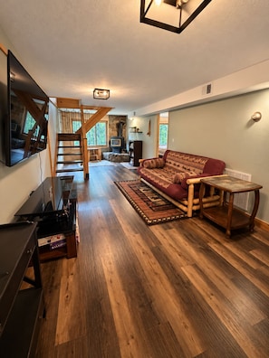A spacious living area with a wooden floor, a sofa, a television, and a staircase leading to another level. - Stunning Luxury Chalet with Attached Garage (Bessemer)