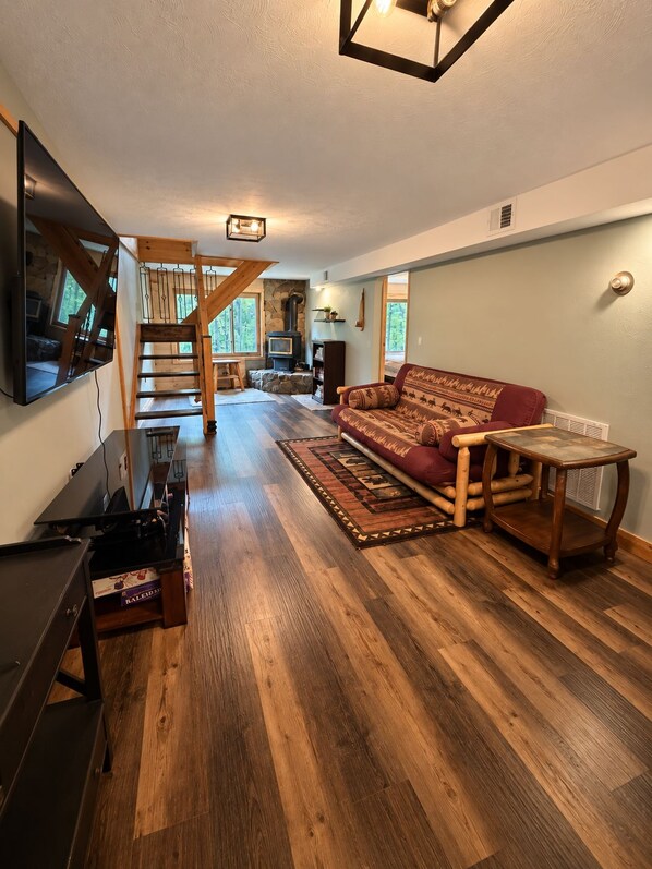 Ein geräumiger Wohnbereich mit Holzboden, einer Couch, einem Fernseher und einer Treppe, die zu einer anderen Ebene führt.