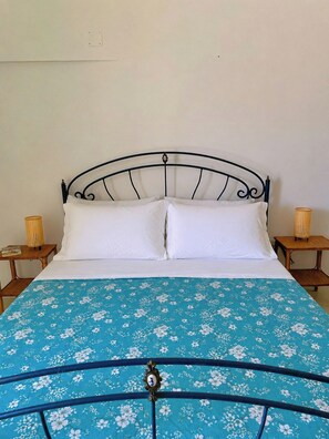 Una cama con estructura metálica, ropa de cama blanca y una colcha de flores azules.