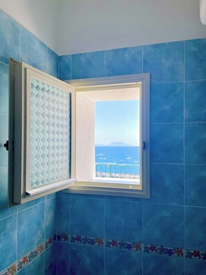 Ein Zimmer mit großem Fenster, blauen Fliesenwänden und Meerblick.
