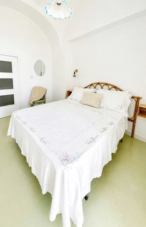Quarto com cama grande, mesa de cabeceira, cadeira, espelho e porta com janelas.