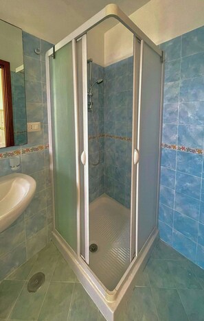 Casa de banho com cabine de duche, lavatório e paredes em azulejo.