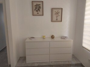 A white dresser with drawers, a framed plant on the wall, and a small vase on the dresser. - Villa Indy (Sainte-Anne)