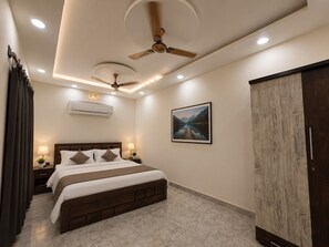 Ein Hotelzimmer mit Bett, Deckenventilatoren, Einbauleuchten, einer Klimaanlage, einem gerahmten Landschaftsbild und einem Kleiderschrank.