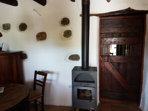 Ein rustikaler Innenraum mit Kaminofen, Holztür und Wand mit Rundvertiefungen.