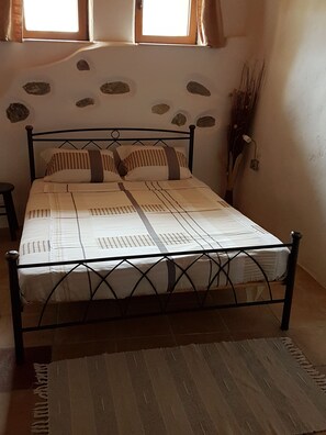 Ein Bett mit Metallgestell, weißer Bettwäsche und einem gemusterten Überwurf.