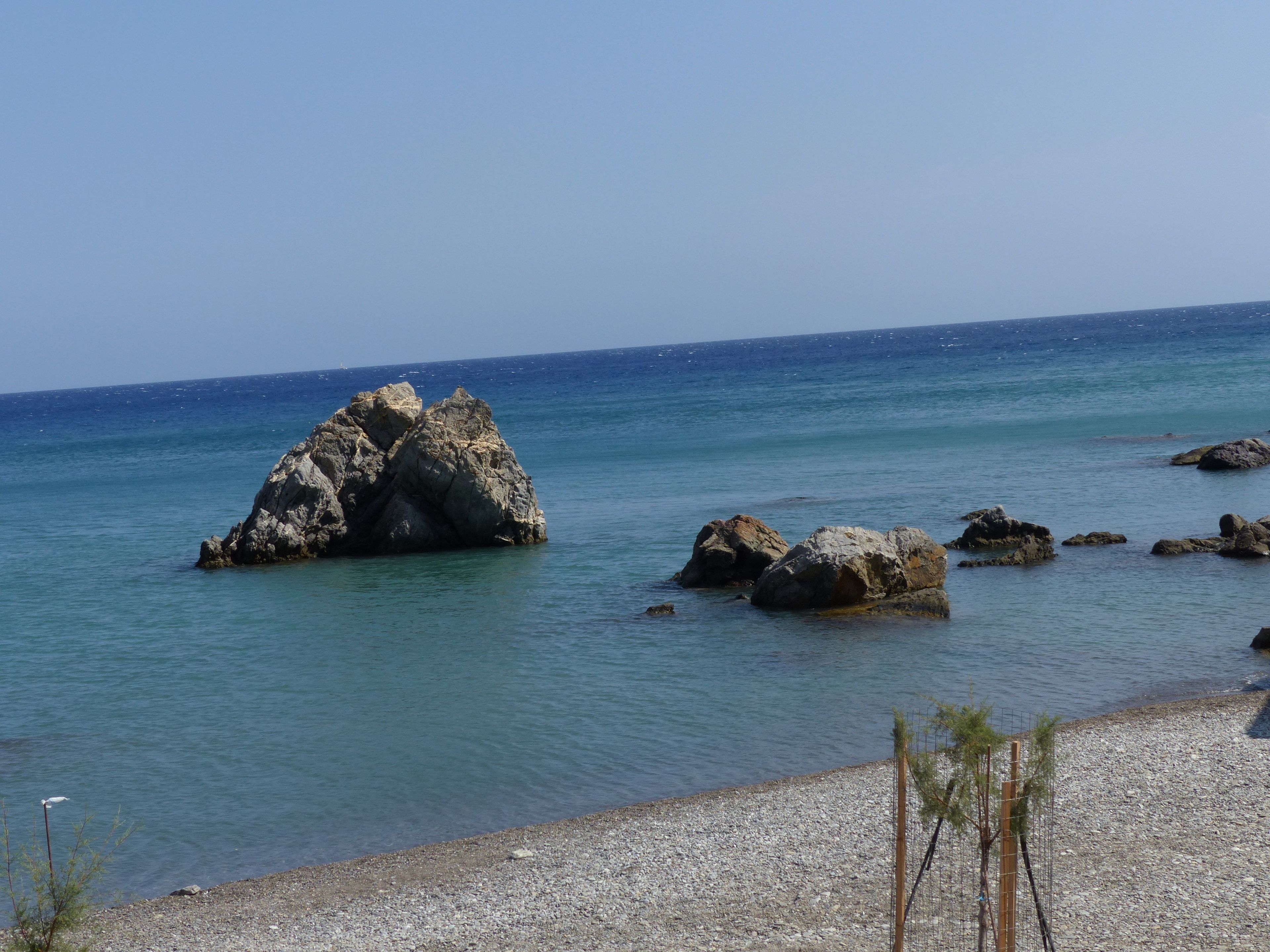 Un littoral rocheux bordé d’une eau d’un bleu limpide et parsemé de quelques petits arbres.