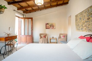 Ein Schlafzimmer mit einem großen Bett, zwei Stühlen, einem kleinen Tisch, einem Holzbüro und einer Steinwand.