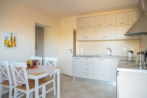 Eine moderne Küche mit weißen Schränken, einer Spüle und einer Arbeitsplatte. Es gibt eine Essecke mit Tisch und Stühlen.