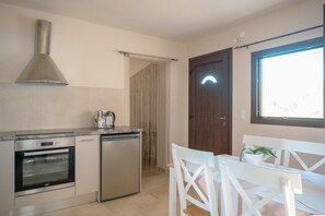 A compact kitchen with a built-in oven, a dishwasher, and a coffee maker. There is a dining area with a table and chairs. - Ferienunterkunft 'Authentic Cretan Escape: Messara Olive Groves & Sunset Views' (Αγία Φωτιά)
