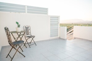 A balcony with two metal chairs, a small table, and a potted plant. - Ferienunterkunft 'Authentic Cretan Escape: Messara Olive Groves & Sunset Views' (Αγία Φωτιά)