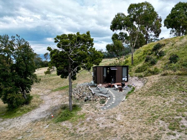 Une cabane moderne dotée d’un patio, entourée d’arbres et bordée d’un sentier de terre.
