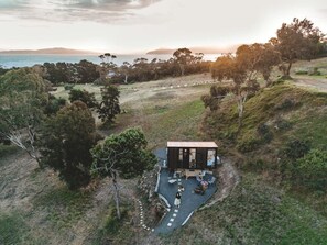 Un chalet isolé doté d’une terrasse, entouré d’arbres et offrant une vue sur l’océan.