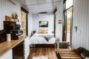Une chambre à coucher de taille réduite, comprenant un lit, une table de chevet et une vue sur l’extérieur grâce à une porte coulissante.
