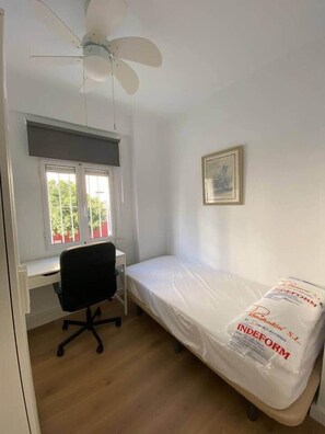 A bedroom with a single bed, a desk with a chair, a ceiling fan, and a window with blinds. - Nalón Apartments Seville (Seville)