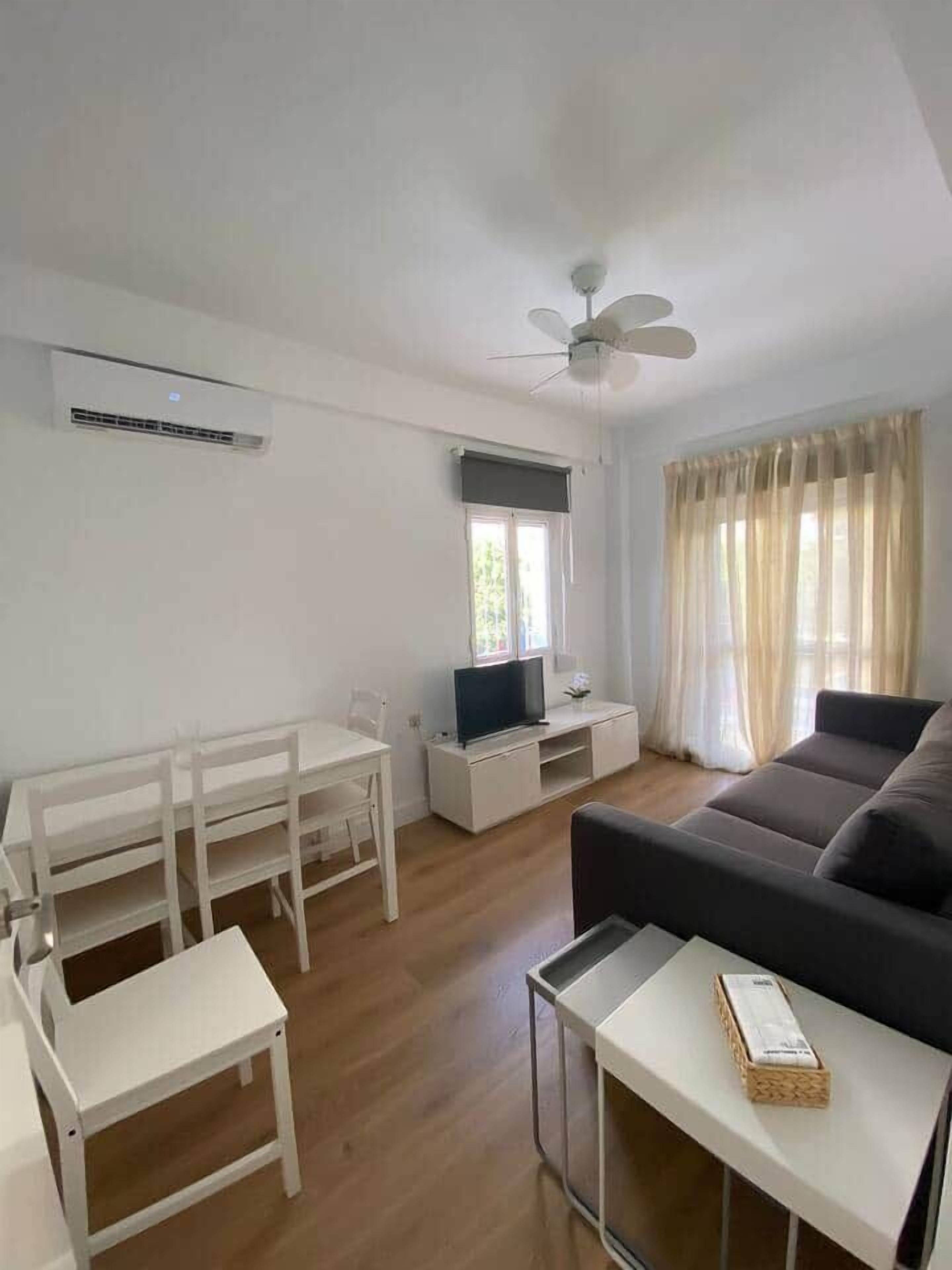 Un salon comprenant un canapé, un téléviseur, une table à manger avec des chaises, un ventilateur de plafond et une fenêtre avec des rideaux.