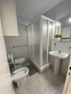 Et badeværelse med toilet, bidet, håndvask og en bruseniche med glasvægge.
