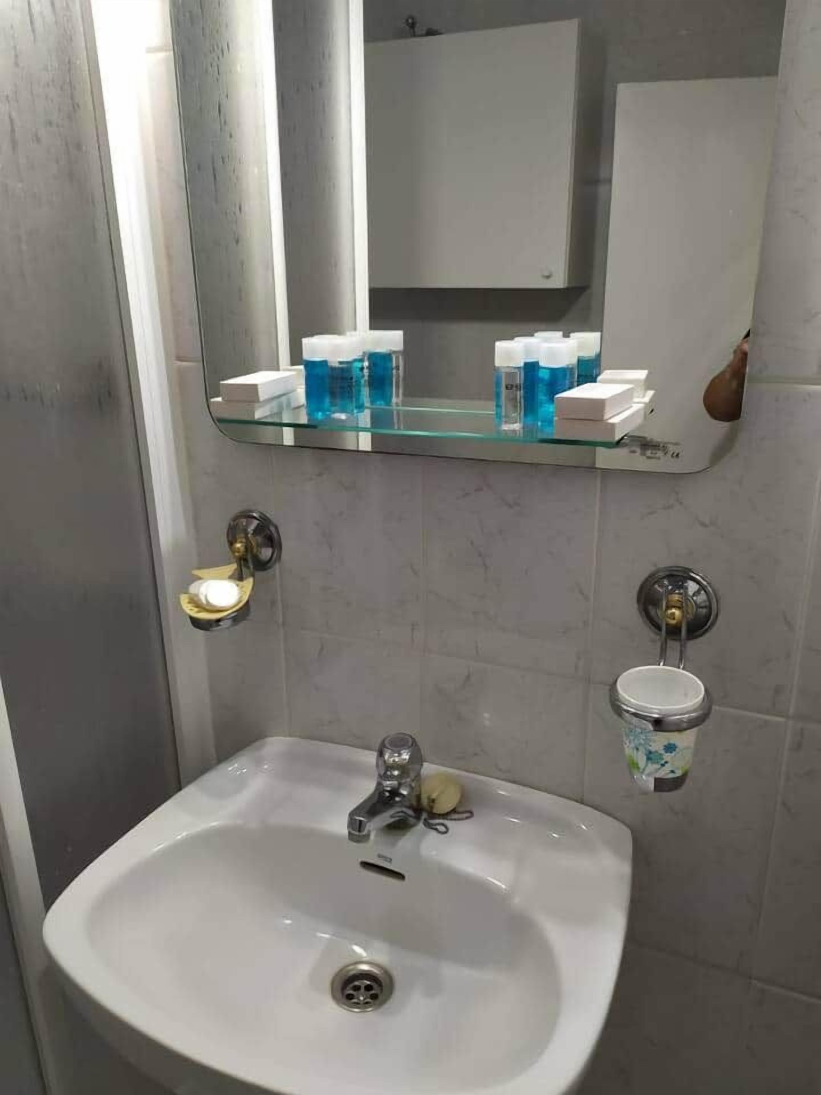 A bathroom with a white sink, a mirror above it, and a shelf with toiletries.