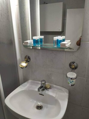 A bathroom with a white sink, a mirror above it, and a shelf with toiletries. - Nalón Apartments Seville (Seville)