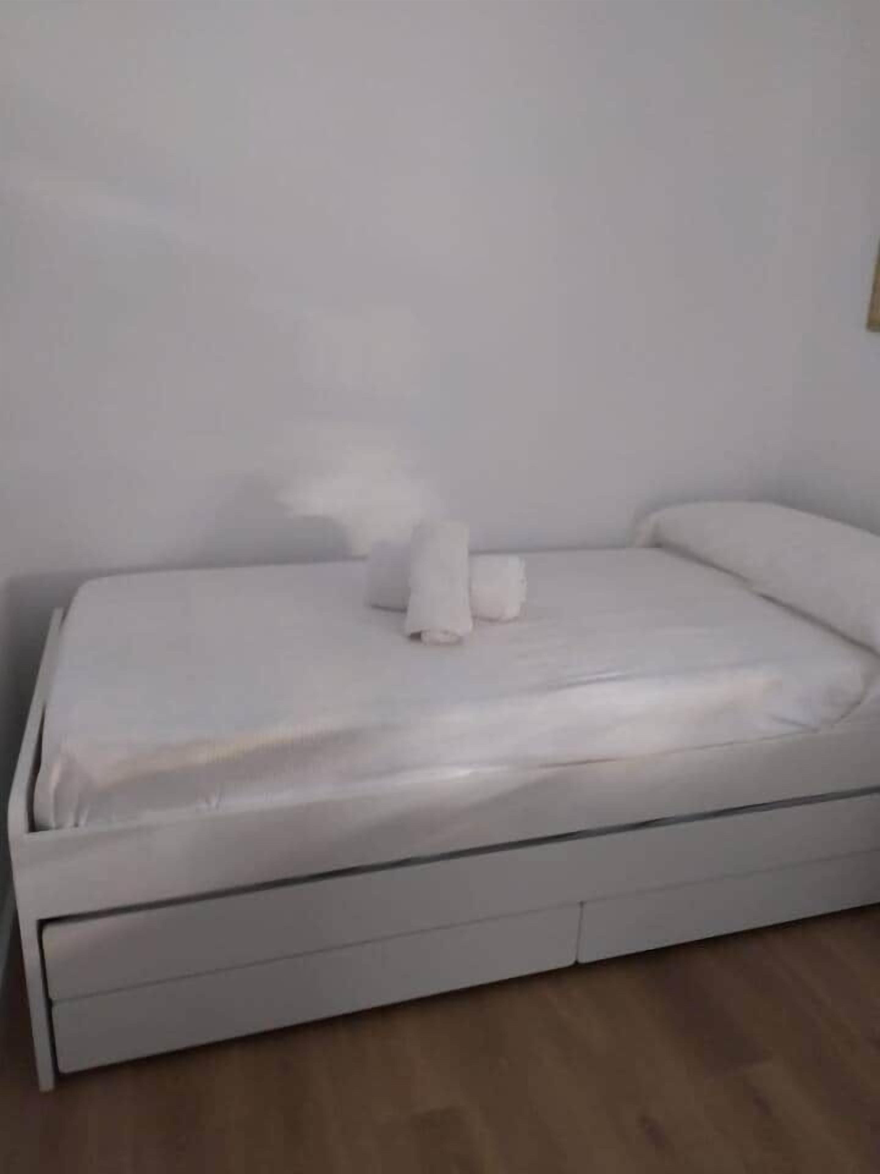 A single-bed room with a white mattress, pillows, and a wooden floor.