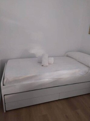 A single-bed room with a white mattress, pillows, and a wooden floor. - Nalón Apartments Seville (Seville)