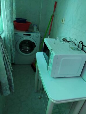 A compact laundry area with a washing machine, a microwave, and a table with a basket. - Nalón Apartments Seville (Seville)