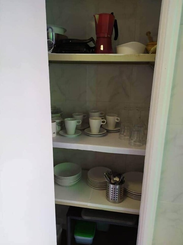 Et køkken med hylder fyldt med tallerkener, kopper og en kaffemaskine.