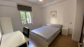Ein Schlafzimmer mit Bett, Schreibtisch, Stuhl, Deckenventilator, Fenster und Nachttisch.