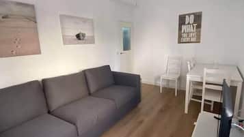 Ein Wohnzimmer mit grauem Sofa, einem weißen Tisch, einem Deckenventilator und einer Wand mit einem motivierenden Zitat.