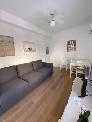 En stue med en grå sofa, et hvidt bord, en loftsvifte og en væg med et motiverende citat.