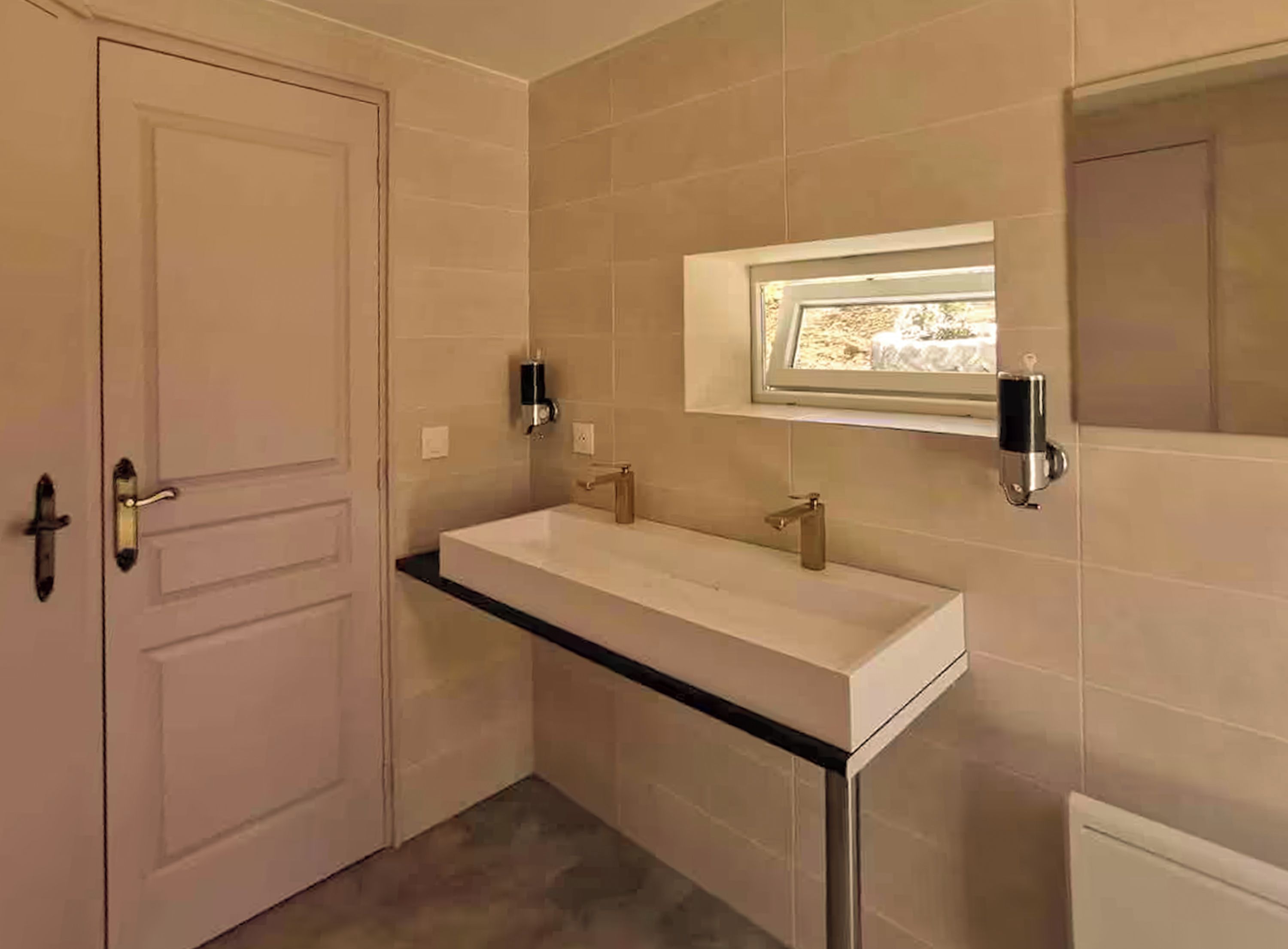 Ein Badezimmer mit einem weißen Waschbecken, zwei Wandleuchten und einem Fenster über dem Spiegel.