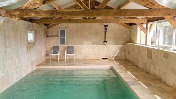 An indoor swimming pool with a stone wall, wooden beams, and two chairs. - Manoir de la Désirée: 15–25 guests, pool, service (Saint-Désir)
