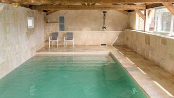 Une piscine intérieure avec un mur en pierre, des poutres en bois et deux chaises.