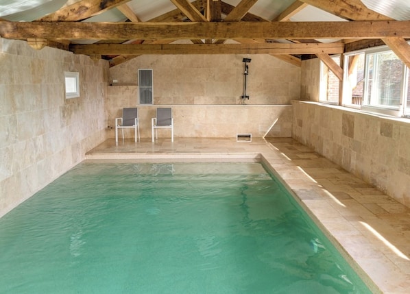 Une piscine intérieure avec un mur en pierre, des poutres en bois et deux chaises.