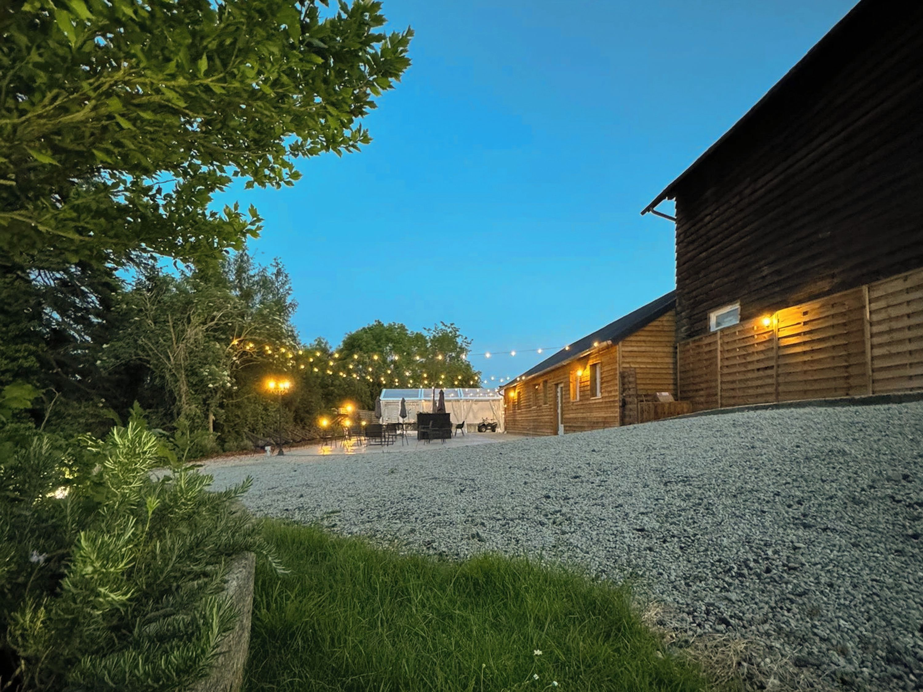Een rustiek houten gebouw met een grindpad, omringd door bomen en lichtjes.