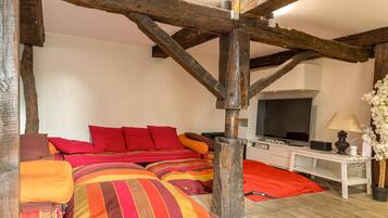 A bedroom with a sloped ceiling, wooden beams, a bed with colorful bedding, a television, and a bedside table with a lamp.