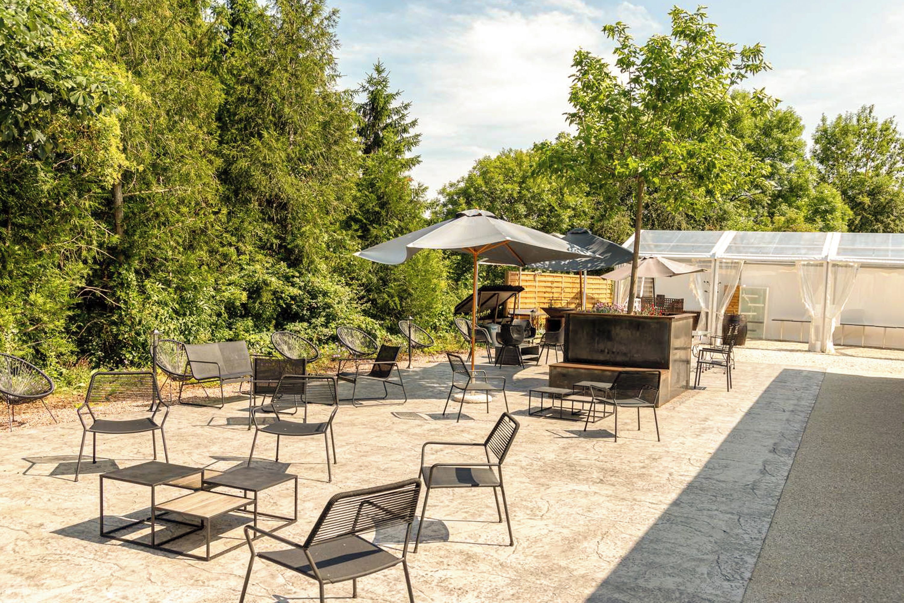 Een terras buiten met metalen stoelen en tafels, een barbecuegrill, en een overdekte zithoek.